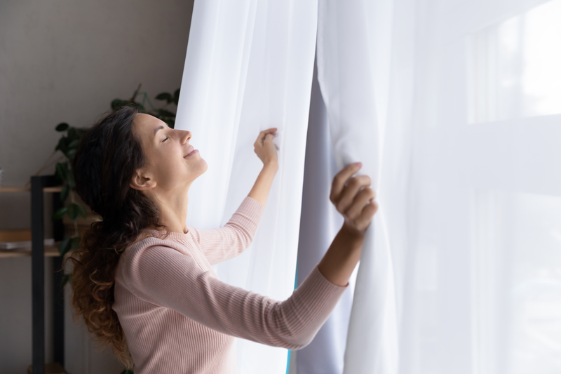 Woman Opening White Curtains on a summer's day